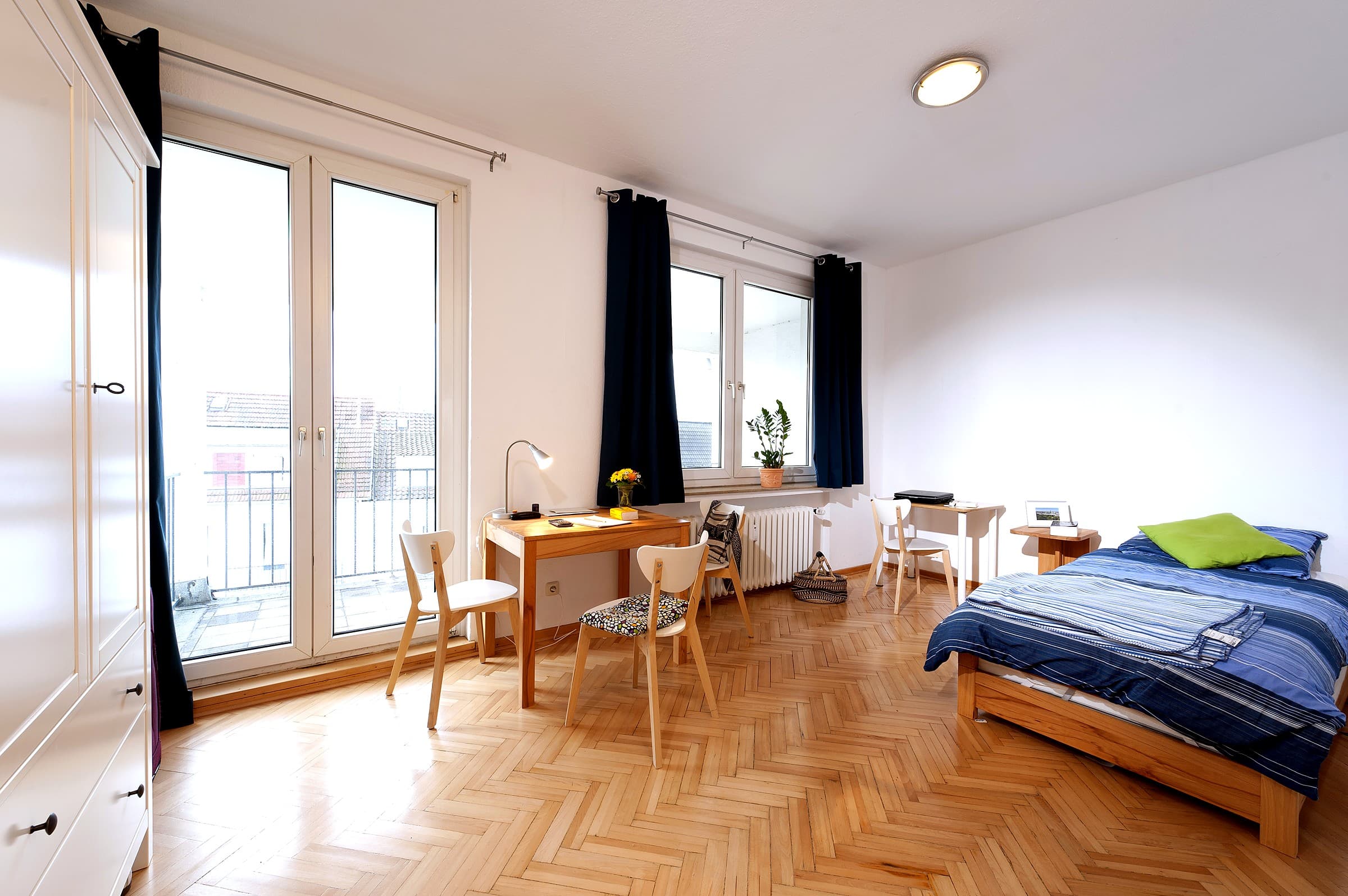 bright student room with a bed, desk, and balcony doors